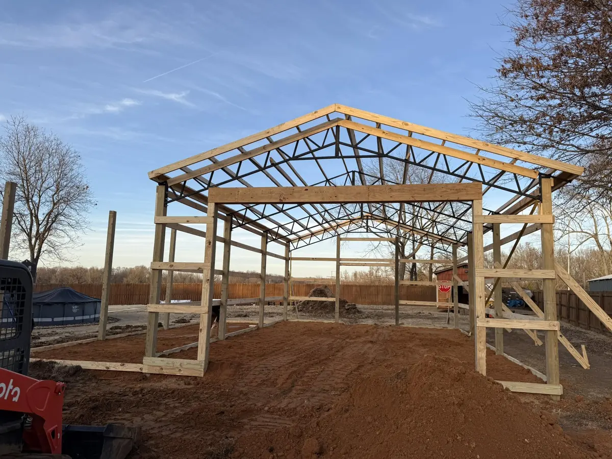 Pole barn frame with steel trusses under construction on a bright day