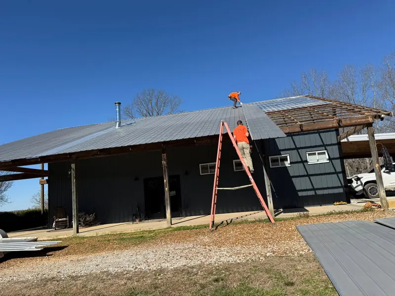 Crew member on a ladder installing metal roofing on a dark-sided building